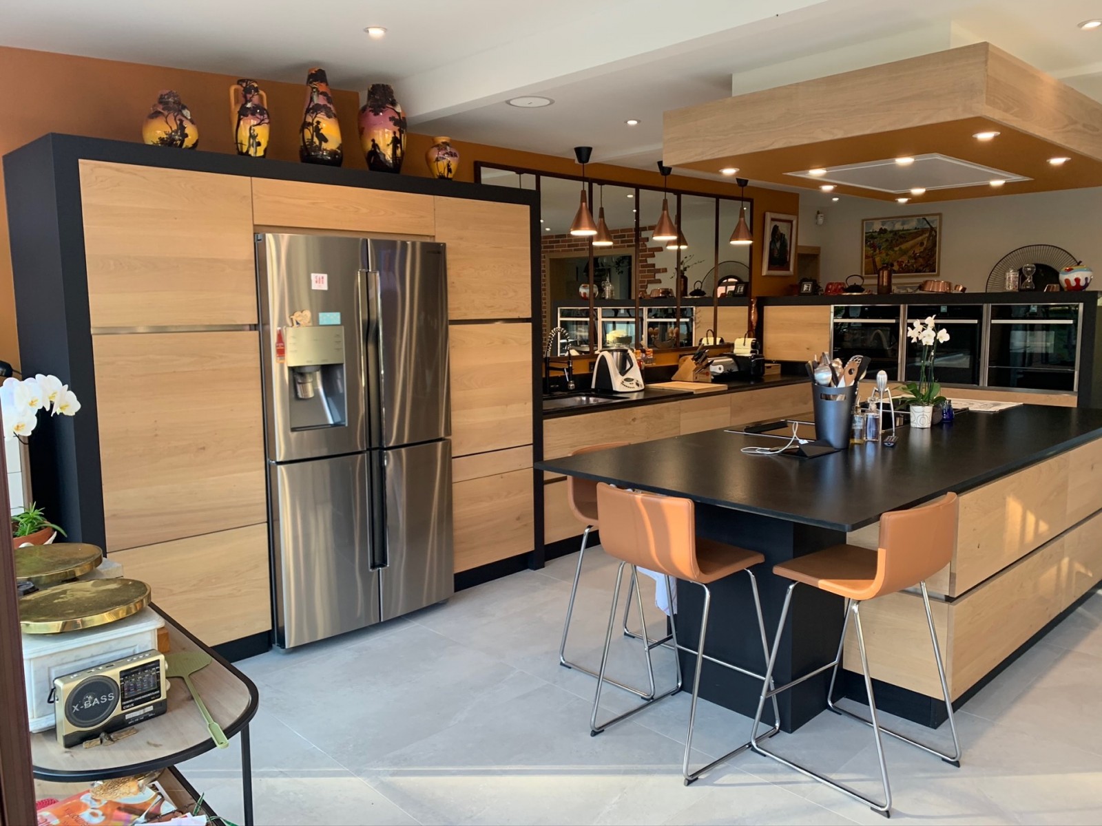 Une cuisine noire et bois avec grande verrière miroir et frigo américain, fabriquée sur mesure et installée près de Paris